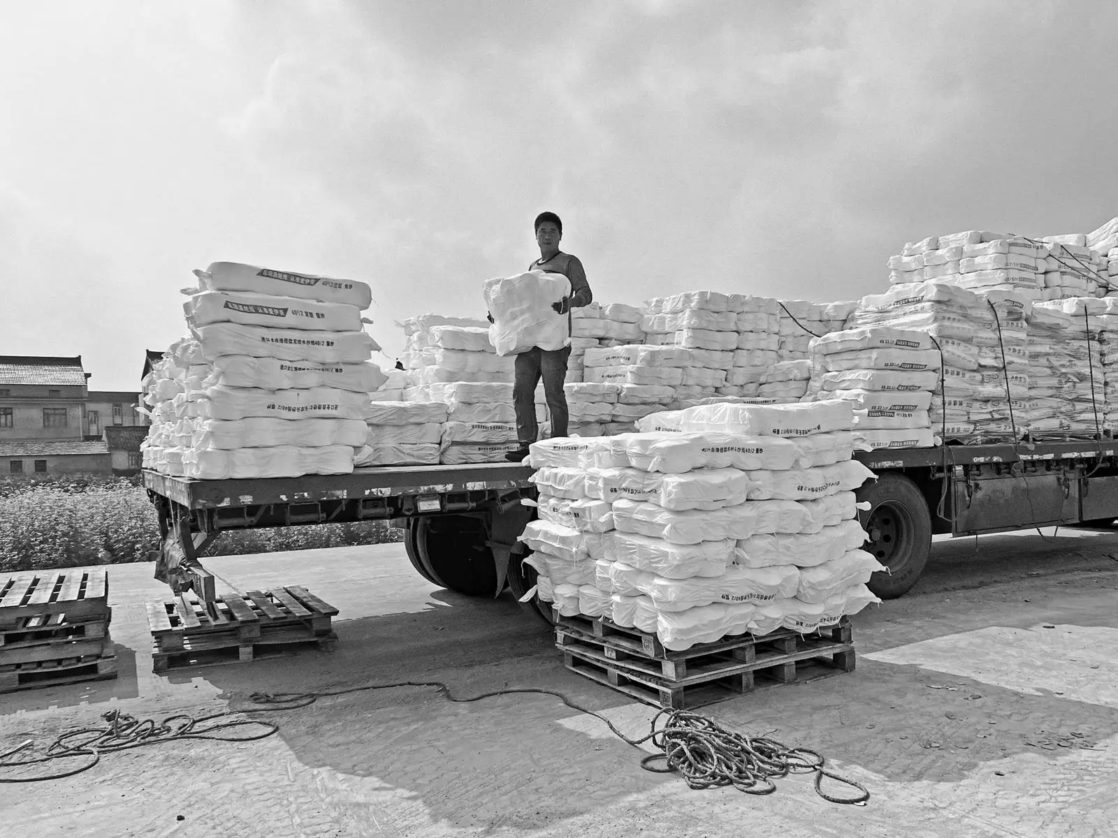 A worker stacking pressed bales of white PP woven bags on a flatbed truck