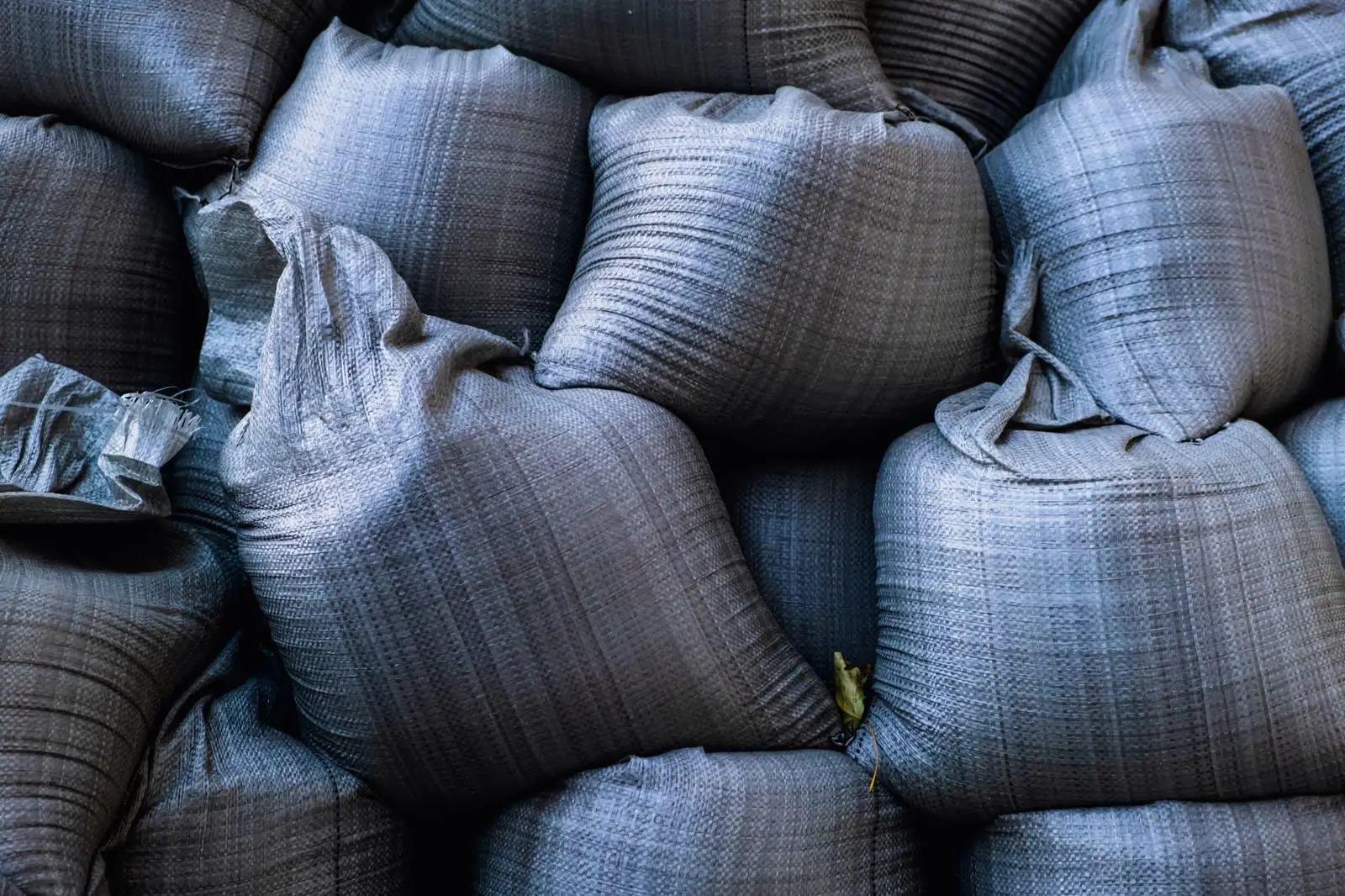 Close-up of grey woven polypropylene fabric — the criss-cross weave that gives a bag its strength